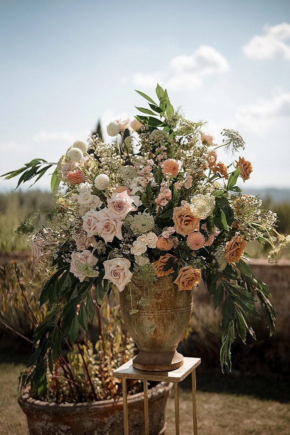 Wedding floral arrangement in a ceremony floral urn with roses, baby’s breath, and greenery on a pedestal against open sky