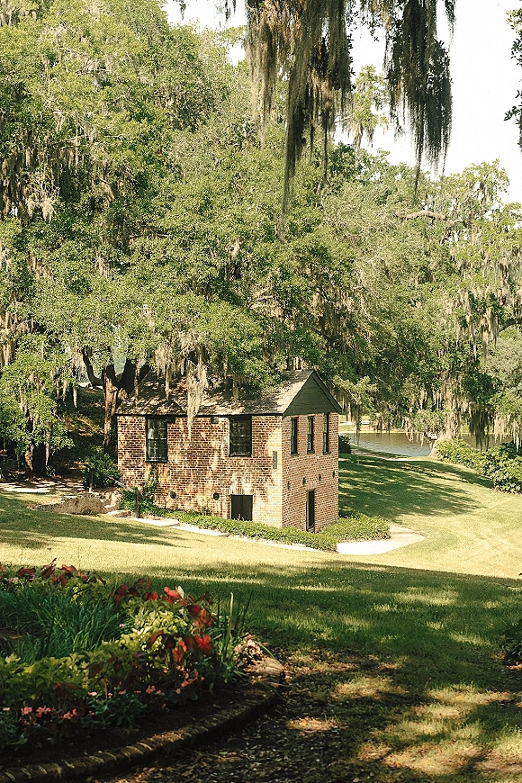 Garden wedding venue with outdoor wedding venue lawn, oak trees draped in moss, paved garden path, and a brick building by the lake