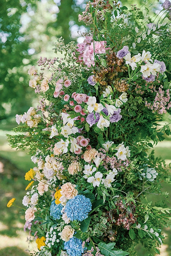 Wedding floral arrangement with hydrangea and roses on a ceremony floral pillar, styled with greenery on an outdoor garden lawn with trees