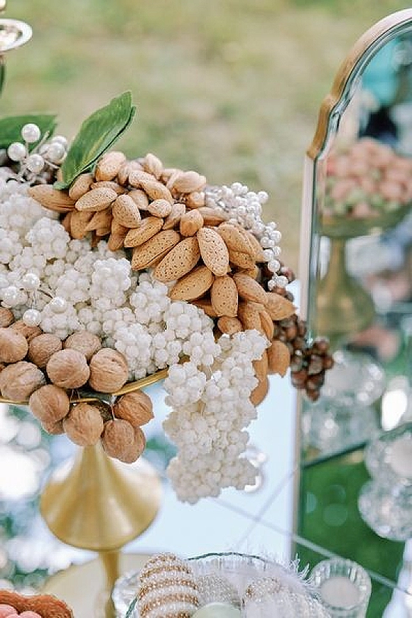 Wedding tablescape with a wedding centerpiece arrangement of white flowers, almonds and walnuts, pearl garland, and gold vase on a mirror tray outdoors