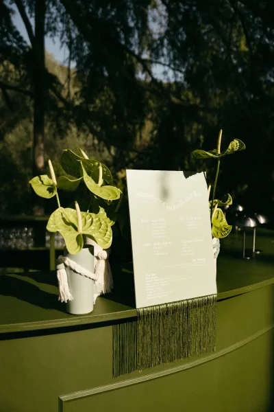 Cocktail menu sign doubling as a signature drink sign, accented with an anthurium, set against trees in an outdoor setting.