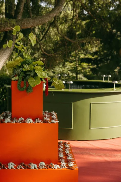 Reception decor with an outdoor reception bar anchored by a circular bar, set beneath garden trees and arching branches.