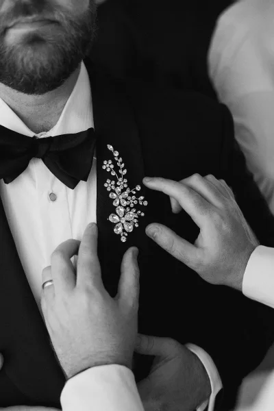 Groom boutonniere styled as a refined brooch boutonniere, pinned to a classic tuxedo lapel, securely fastened and neatly framed.