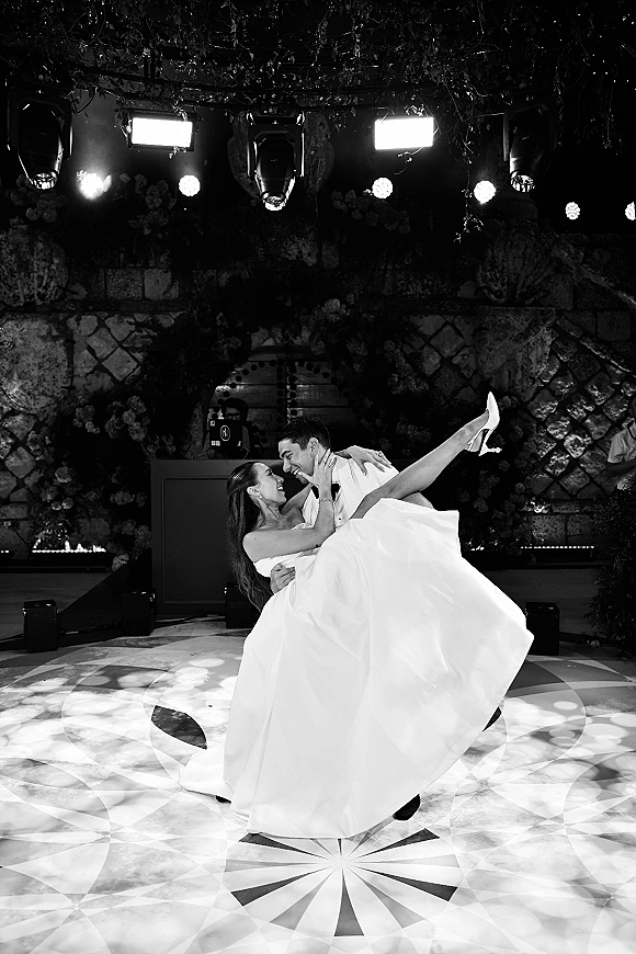 First dance moment as groom lifts bride in a dip, her veil and strapless ballgown flowing under stage lighting on a patterned floor