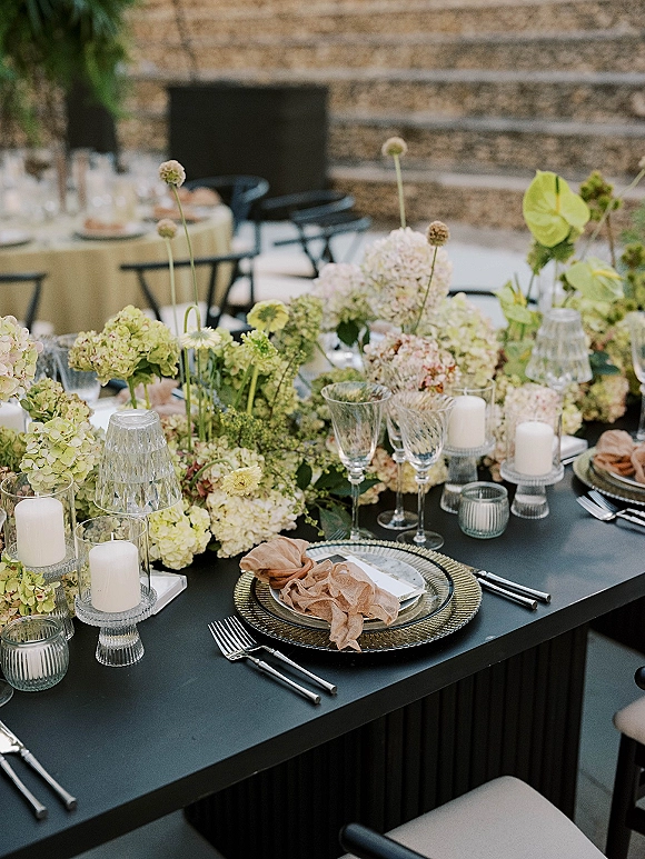 Reception tablescape with black wedding table styling, hydrangea and anthurium centerpiece, candles and crystal glassware on an outdoor patio