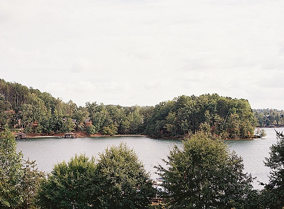Lake landscape with calm water and a tree line across the shoreline, with boat docks under an overcast sky in the distance
