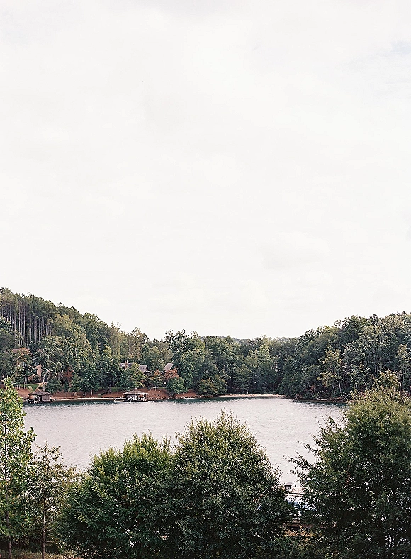 Lake landscape with a wooded lake view, calm water reflecting tree-lined shoreline, docks and distant lakeside homes under an overcast sky