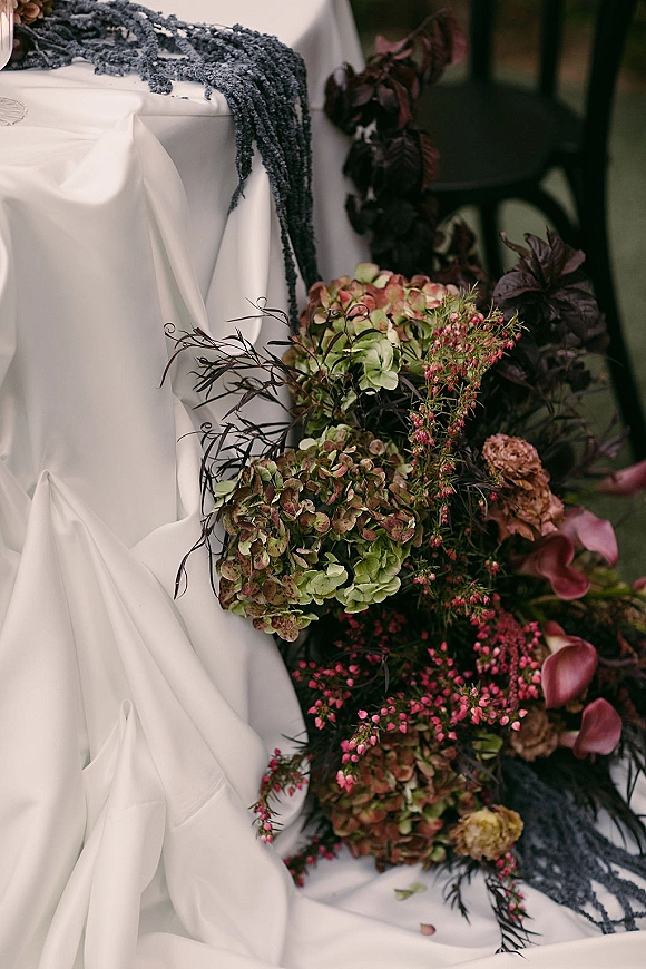 Bridal bouquet with hydrangea wedding bouquet blooms, calla lilies, greenery and berry sprigs, wrapped in white drape and black lace indoors