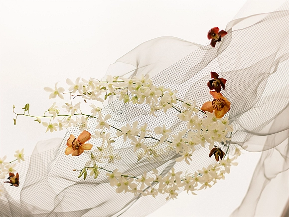 Bridal veil detail with sheer tulle and floral appliques, featuring white embroidered flowers and orange orchid accents on a white backdrop