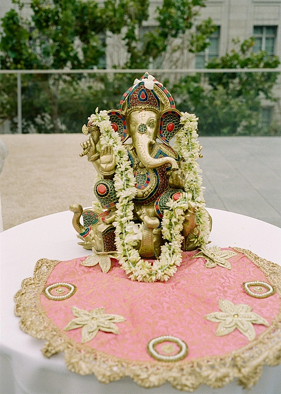 Ganesha wedding decor featuring a ganesha statue decor with flower garland on embroidered cloth with gold trim on an outdoor terrace