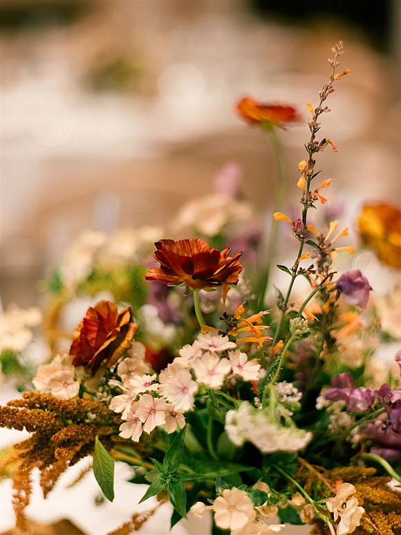 Wedding centerpieces with wildflower wedding centerpiece blooms in orange, cream, and purple greenery on a reception table with bokeh lights