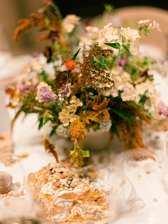 Wedding centerpiece with a wildflower centerpiece in a ceramic bowl, featuring dried foliage and blush, orange, and white blooms on a white tablecloth