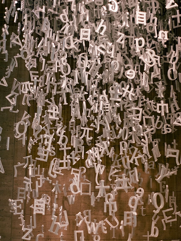 Hanging letter installation with hanging numbers on strings, forming a minimalist typography curtain against a raw concrete wall backdrop
