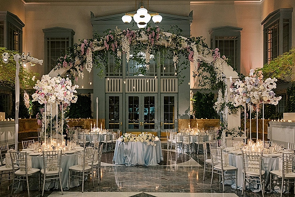 Reception decor with wedding reception design featuring hanging florals and candlelit round tables beneath chandeliers in an indoor courtyard