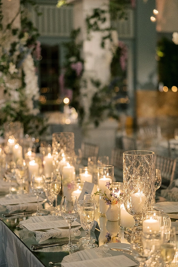Reception tablescape with a candlelit wedding table featuring pillar and votive candles, greenery garland, and place settings in a dining room