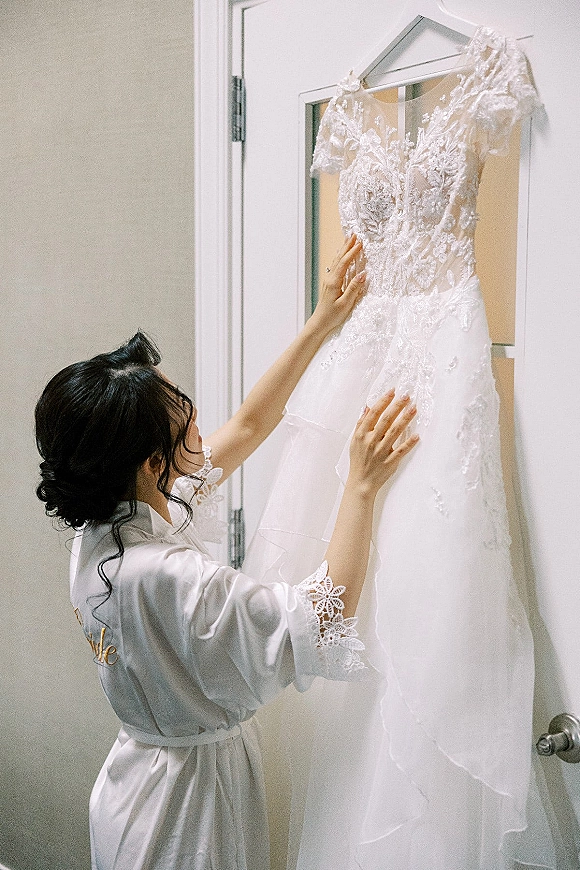 Wedding dress, lace wedding dress hanging on a hanger from a white door, with illusion neckline and tulle skirt in an indoor room