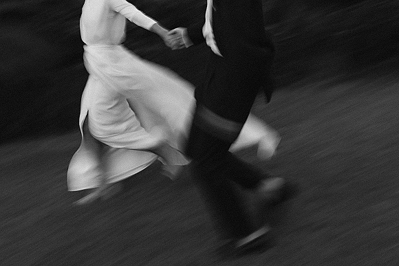 First dance as bride in a wedding dress and groom in suit hold hands on the dance floor, her dress twirling with dress shoes visible
