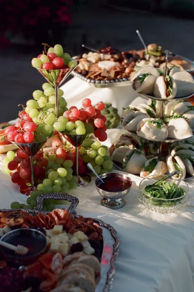 Wedding grazing table laden with cocktail hour appetizers, featuring grapes, set on a white tablecloth amid garden foliage