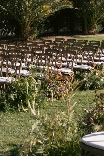 Ceremony aisle decor for outdoor ceremony seating, featuring crossback chairs on a lawn under palm trees.