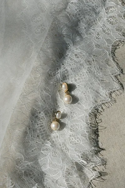 Pearl bridal earrings, graceful gold pearl drop earrings arranged with a lace accent, their warm sheen capturing timeless bridal elegance.