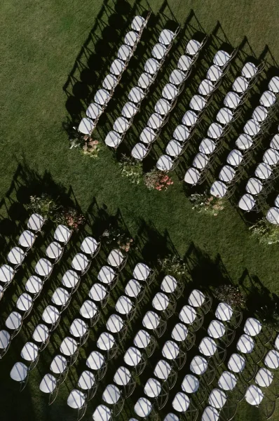 Ceremony seating arranged in an outdoor ceremony layout with crossback chairs flanking a wide center aisle on a grass lawn.