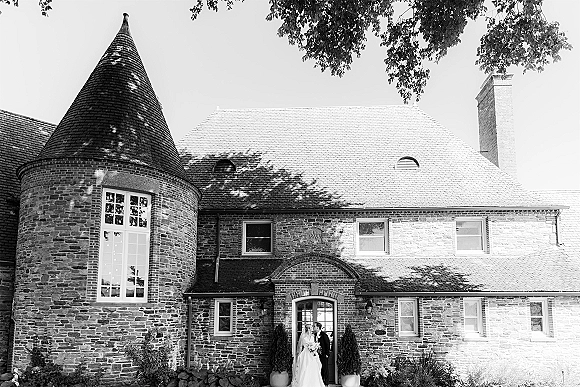 Wedding couple portrait in black and white of bride and groom kissing in a brick arch doorway, her veil and bouquet framed by potted plants