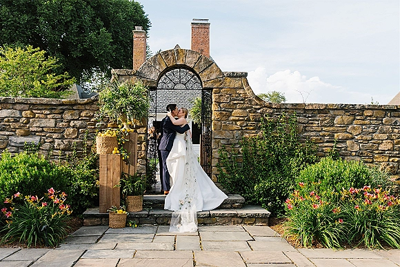 Wedding kiss portrait of bride and groom kissing on stone steps, long veil flowing by a wrought iron gate with lemon décor accents