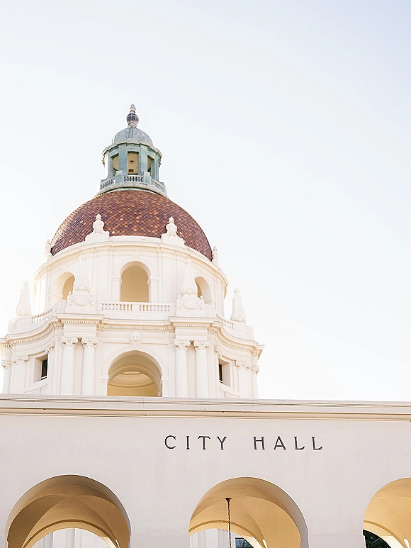 City hall wedding venue with domed roof and arched colonnade, exterior signage visible against a bright white sky backdrop