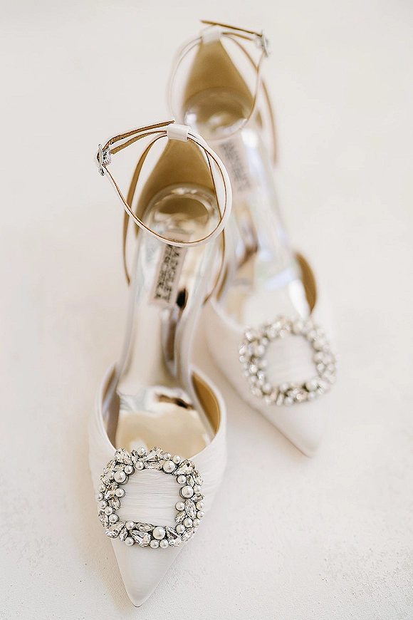 Bridal shoes, white wedding heels with pearl embellishments and rhinestone buckles, pointed toe ankle straps on light fabric surface