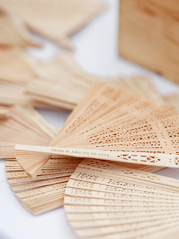 Wedding favor fans with personalized wedding fans engraving, wooden folding design and laser-cut pattern on a white tablecloth over wood surface