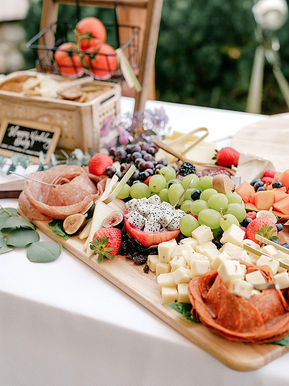 Wedding charcuterie board and wedding grazing board with cheese cubes, salami, berries, figs and fruit on a wood board with eucalyptus accents outdoors
