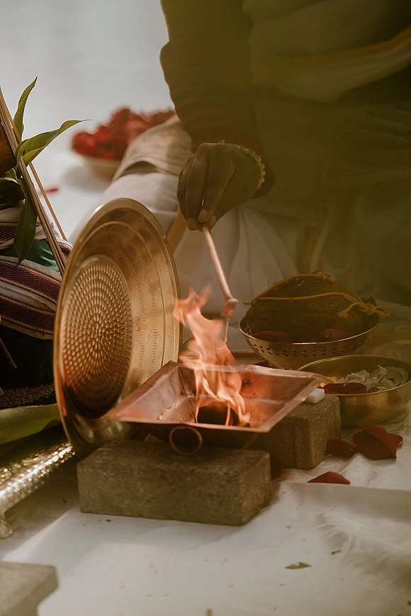 Wedding ritual fire burning in a metal bowl on brick base with havan kund wedding offerings, brass plate, incense, petals and banana leaves