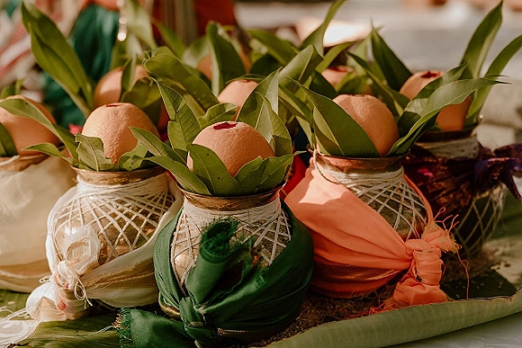 Wedding favor display of glass jars with citrus wedding favors, twine wraps, green leaves and ribbons arranged on a table in soft indoor light