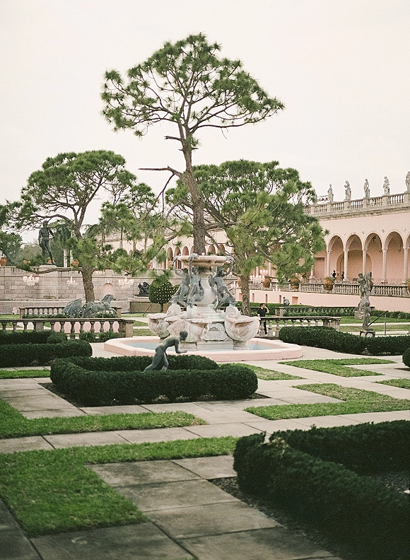 Garden fountain at a wedding venue garden with statues and trimmed hedges, bordered by a stone balustrade under string lights