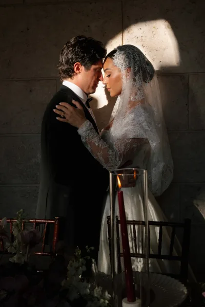 Couple portrait of a bride and groom embrace, foreheads gently touching before a rustic stone wall, her bridal veil softly framing them.