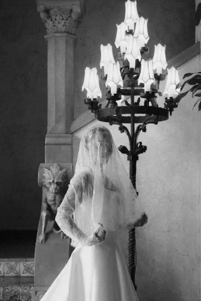 Bridal portrait in black and white of a bride with a lace veil on a stone staircase beside a wrought iron lamp and gargoyle.