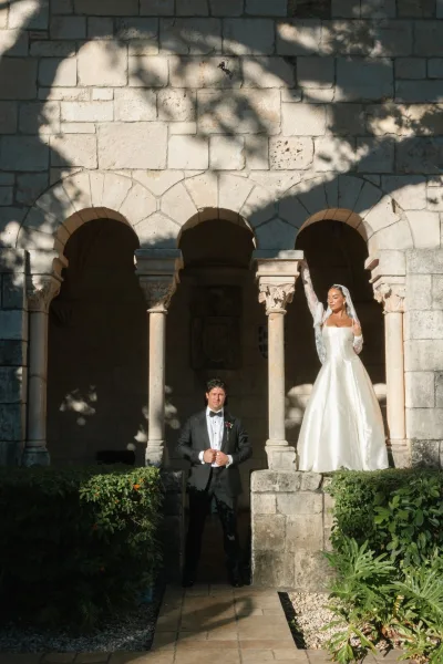 Couple portrait featuring a mantilla veil bride beside her groom beneath stone arches framed by garden greenery.