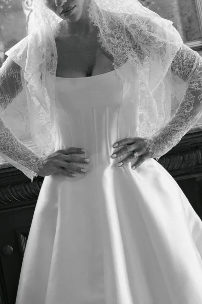 Wedding dress close-up of a strapless bridal gown, hands at the waist, showing a lace veil edge against a carved wood mirror frame.