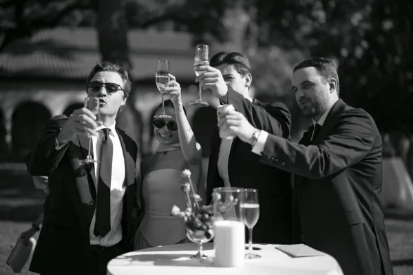 Wedding champagne toast during cocktail hour toast, guests raise champagne flutes in a garden courtyard with arches.