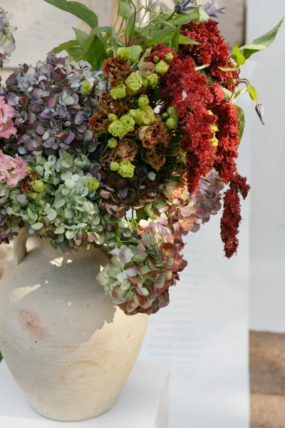 Floral arrangement in a ceramic urn, elegant wedding flowers set against a stone wall with white signage