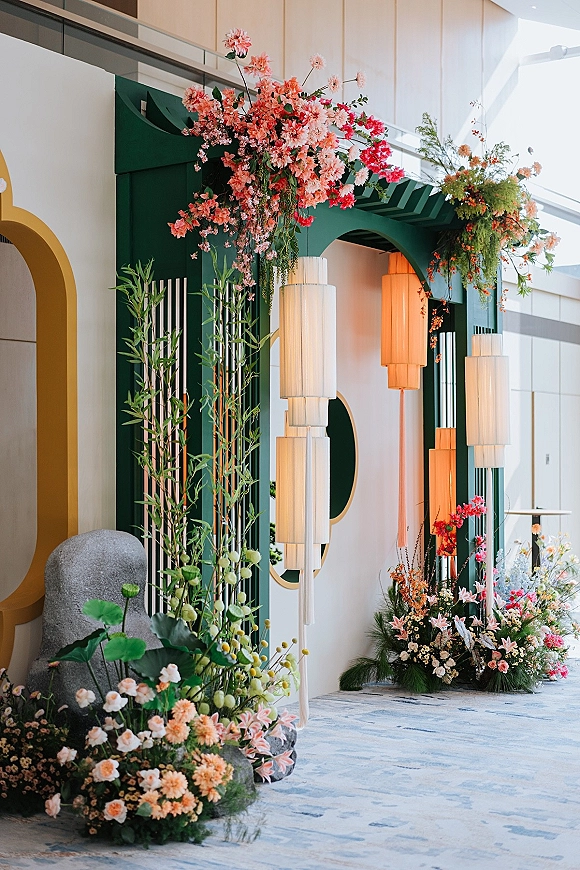 Wedding ceremony backdrop with a modern ceremony arch, lush floral installations and hanging lanterns, set in a high-ceiling indoor venue