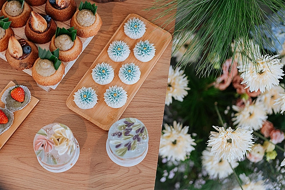 Wedding dessert table with assorted mini cakes and cupcakes on bamboo trays, topped with strawberries and blueberries in a garden setting