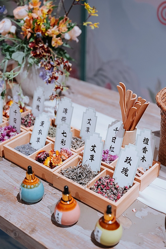 Wedding tea bar with wooden display trays, labeled herbs and glass dropper bottles, arranged on a wood table with dried flowers