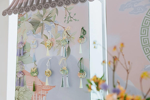 Wedding favors display with hanging wedding favors in tassel drawstring pouches on an illustrated panel, softly lit by window light