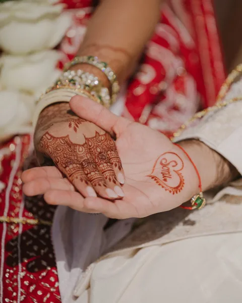 Mehndi hands with bridal mehndi design, intricate henna patterns and green-gold bangles over red embroidered bridal fabric