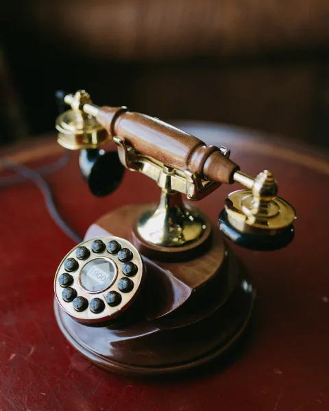 Vintage rotary phone with a wood base and brass handset, rotary dial in focus on a red tabletop against a dark blur background