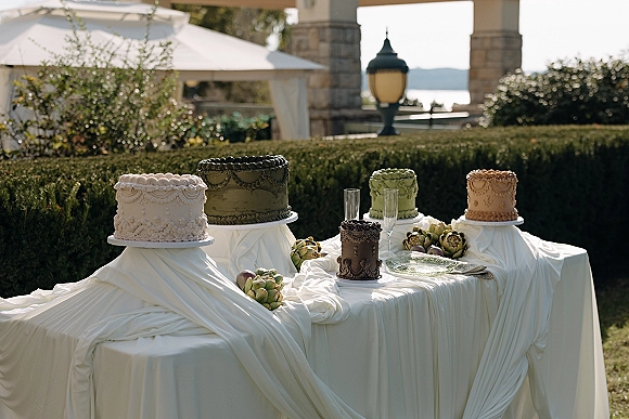 Wedding cake display with assorted cakes on mixed-height stands and champagne flutes on a draped table under a garden tent canopy