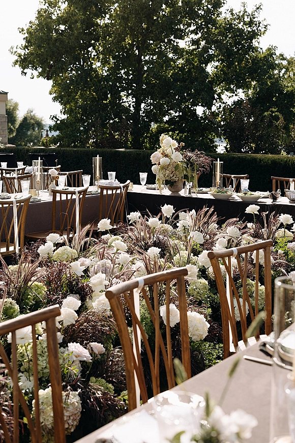 Reception tablescape with an outdoor wedding reception long banquet table, taupe linens, white hydrangeas and roses, taper candles on a terrace by hedges