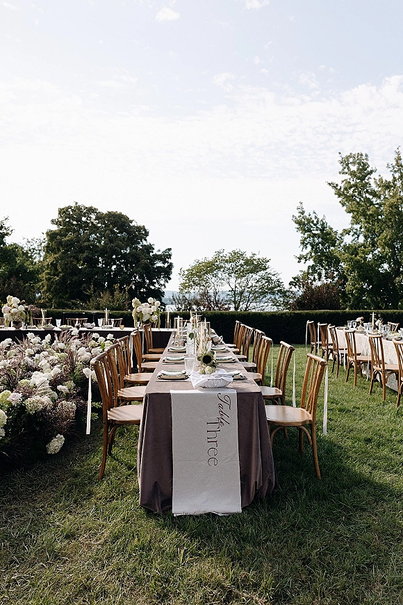 Reception tablescape with outdoor wedding reception tables featuring taper candles, ribbon-tied florals, and layered place settings on a lawn backdrop
