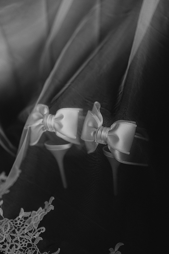 Wedding dress detail with bridal tulle close-up, showing satin bows and lace applique along ribbon trim amid soft fabric folds